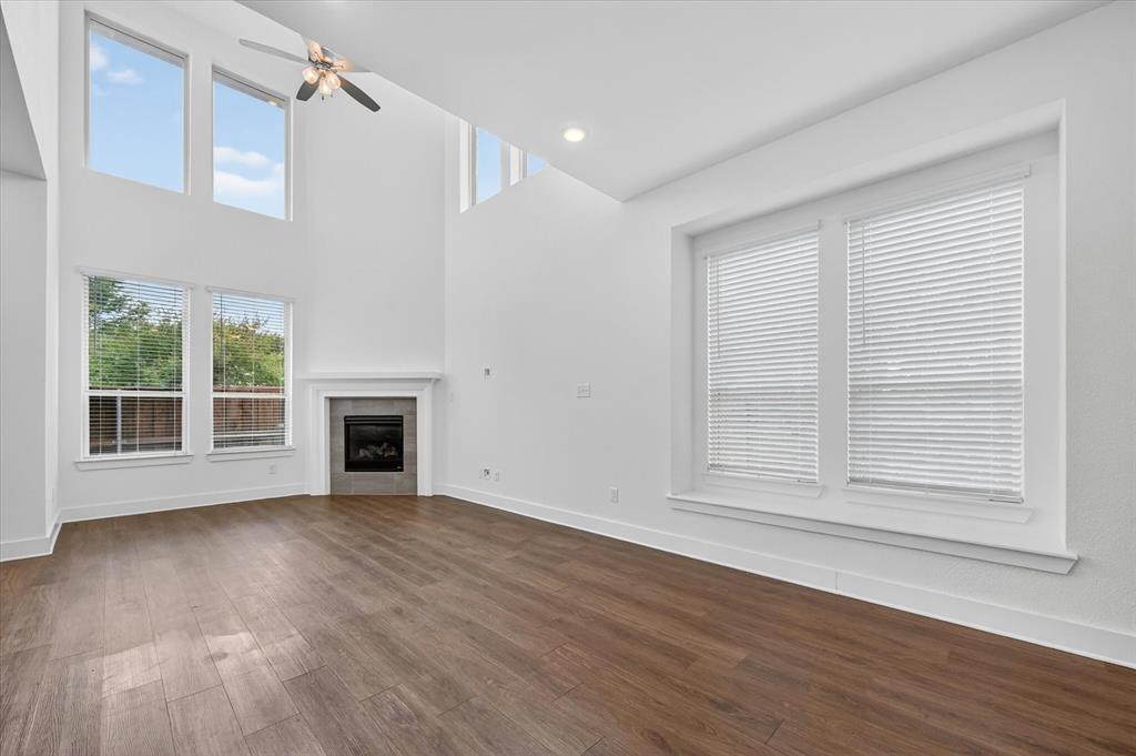 1153 Queensdown Way Forney, TX 75126 - Photo 6 of 26 Spacious living area featuring high ceilings, a contemporary fireplace with tile surround, wood-finish flooring, and multiple large windows with blinds