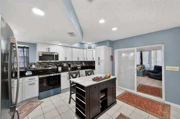 a living room with stainless steel appliances furniture a rug and a kitchen view