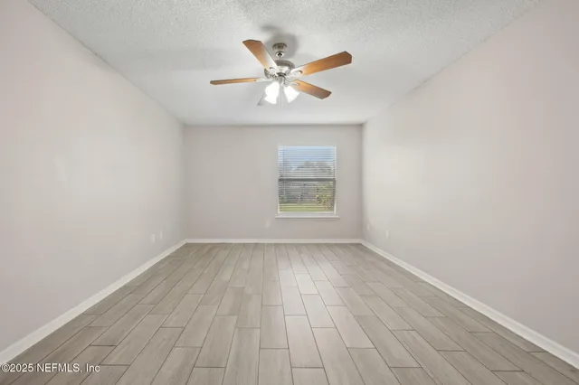 an empty room with wooden floor a ceiling fan and windows