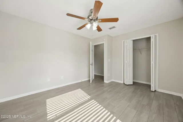 a view of an empty room with wooden floor and a ceiling fan