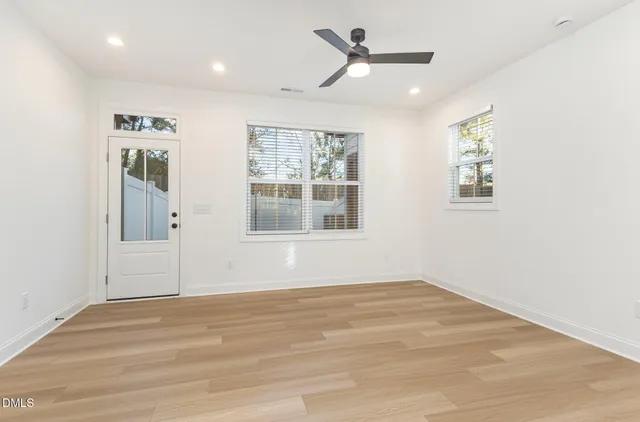 a view of an empty room and a kitchen with a ceiling fan