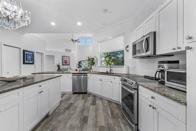 a kitchen with stainless steel appliances granite countertop a sink dishwasher stove and white cabinets with wooden floor