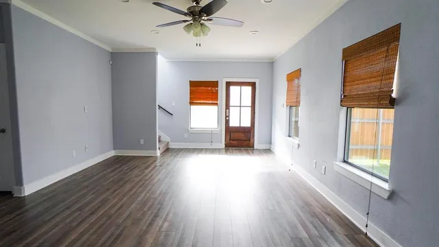 an empty room with wooden floor fan and windows
