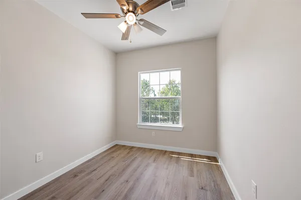 an empty room with wooden floor fan and windows