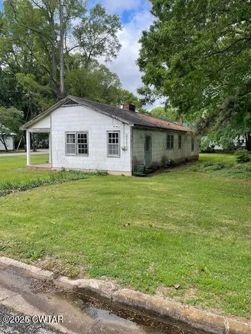 a house that is sitting in the grass with large trees