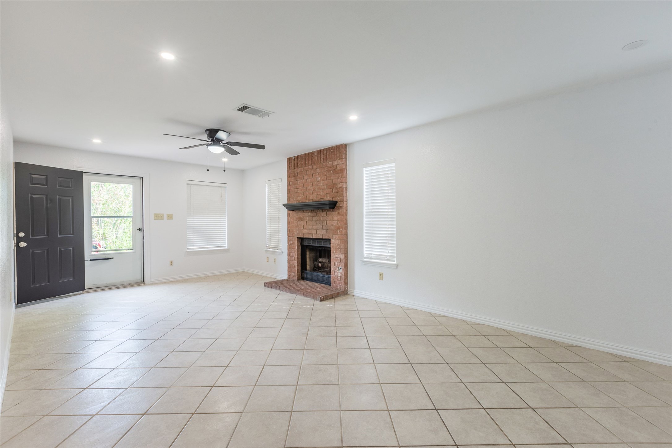 8506 Bisbee Court Austin, TX 78745 - Photo 2 of 20 Spacious living area featuring a brick fireplace with a dark wood mantel, light-toned diagonal tile flooring, and a ceiling fan with integrated lighting
