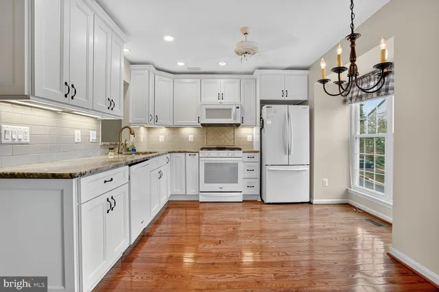 a kitchen with stainless steel appliances granite countertop a refrigerator a sink dishwasher and white cabinets with wooden floor