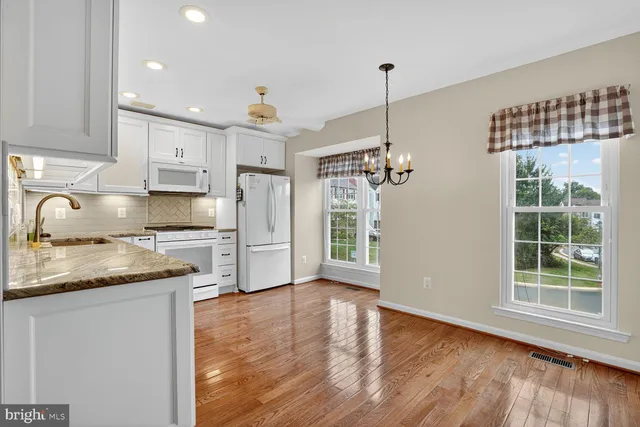 a kitchen with stainless steel appliances granite countertop a sink a stove a refrigerator and white cabinets with wooden floor