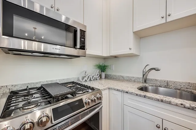 a kitchen with stainless steel appliances granite countertop white cabinets and a stove top oven