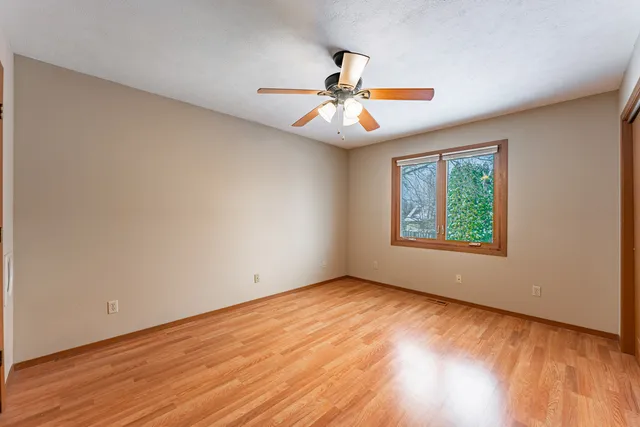 an empty room with wooden floor ceiling fan and windows