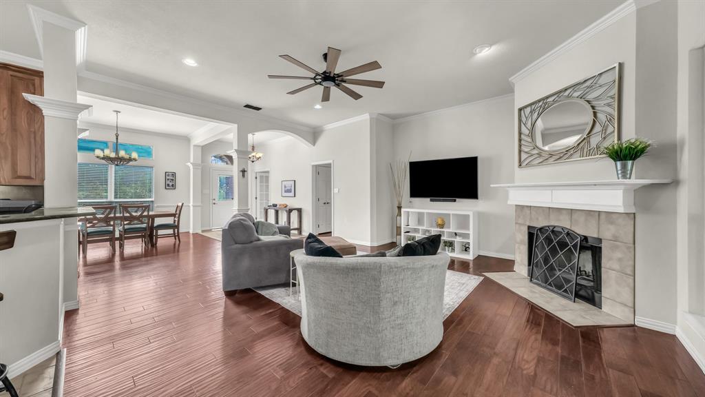 203 Mockingbird Lane Aledo, TX 76008 - Photo 11 of 37 Spacious living area featuring wood-finish flooring, a tiled fireplace with a white mantel, and an open layout to the dining area