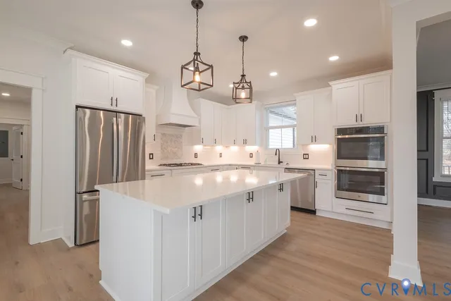 a kitchen with stainless steel appliances kitchen island granite countertop a refrigerator a sink dishwasher a oven and a refrigerator with wooden floor