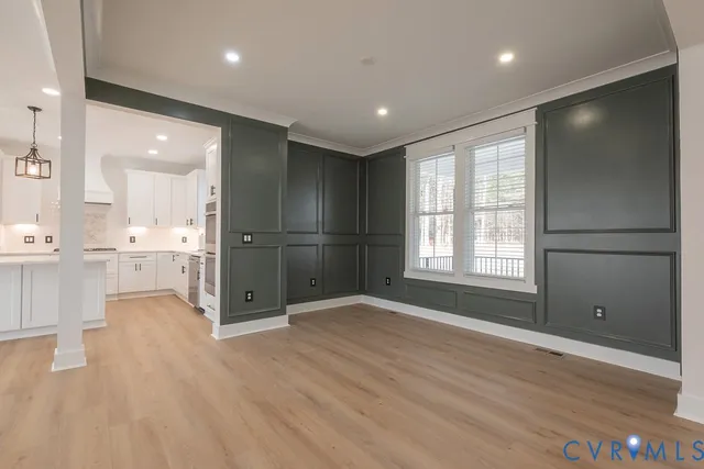 a view of an empty room with wooden floor and a kitchen