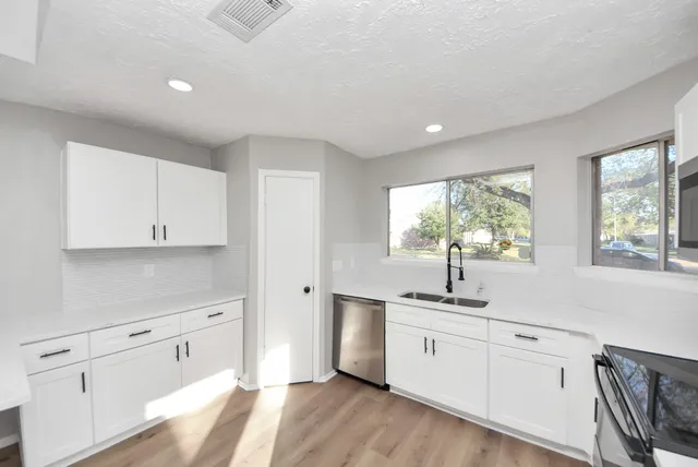 a large white kitchen with granite countertop a stove top oven a sink a refrigerator and white cabinets with wooden floor