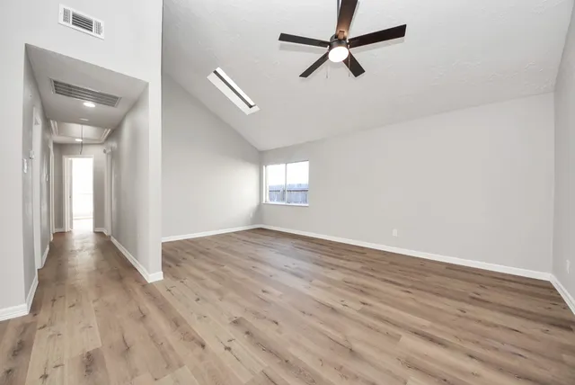 an empty room with wooden floor fan and windows