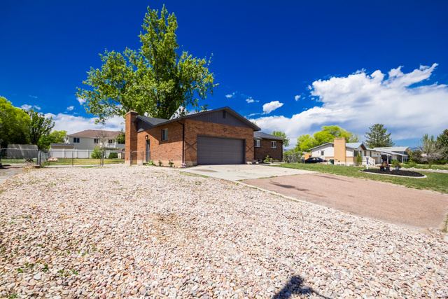634 South 2100th Street West Vernal, UT 84078 - Photo 62 of 71 Brick exterior home with an attached garage, featuring a prominent chimney structure and mature landscaping