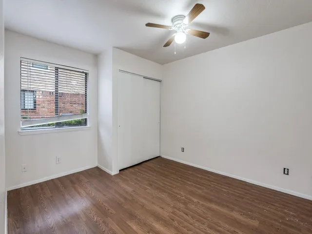 an empty room with wooden floor fan and windows