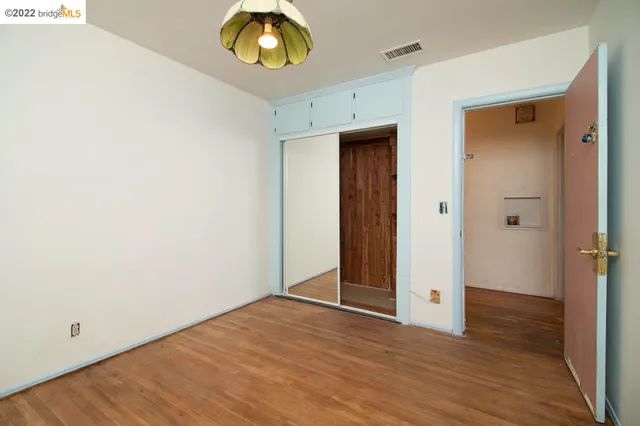 a view of an empty room with wooden floor and closet