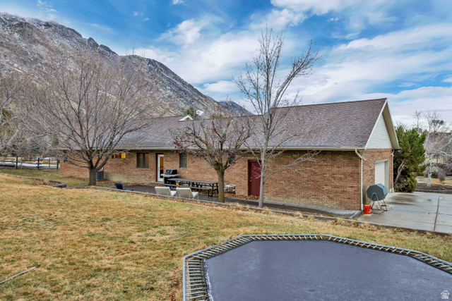 887 Village Way Alpine, UT 84004 - Photo 5 of 28 Back of house featuring a trampoline, a patio area, a yard, a mountain view, and brick siding
