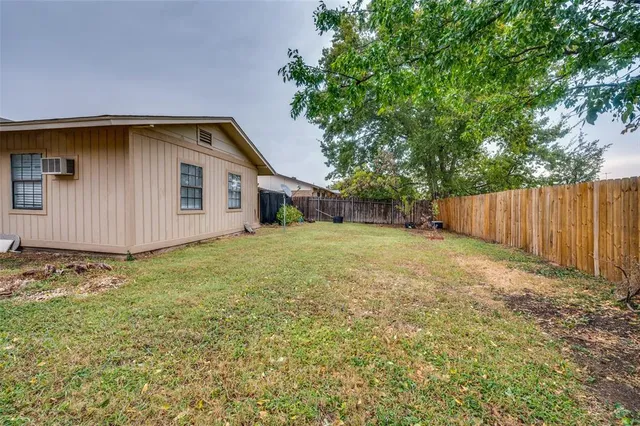 a backyard of a house with large trees and wooden fence