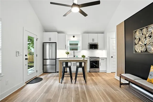 a kitchen with stainless steel appliances a refrigerator a stove top oven a sink dishwasher and white cabinets with wooden floor