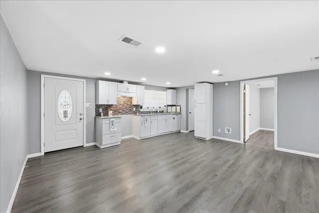 a view of an empty room with wooden floor and kitchen