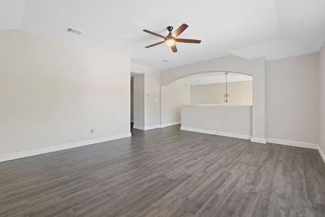 an empty room with wooden floor ceiling fan and windows