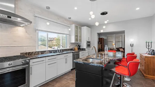 a kitchen with stainless steel appliances granite countertop a stove white cabinets a sink dishwasher and couches with wooden floor