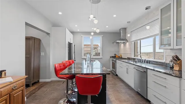 a kitchen with stainless steel appliances kitchen island granite countertop a dining table chairs sink and white cabinets