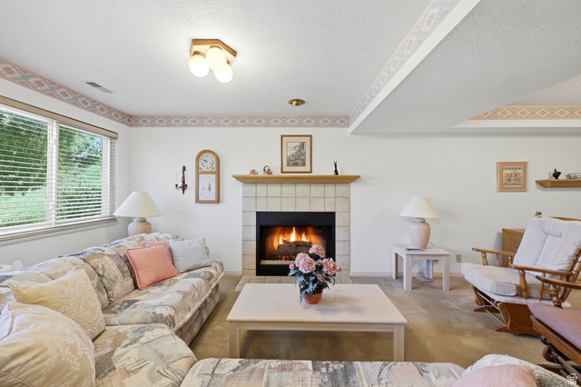 3766 Cardiff Circle Bountiful, UT 84010 - Photo 29 of 46 Carpeted living area featuring a tile-surround fireplace with a wood mantle, multiple windows with blinds, and white walls