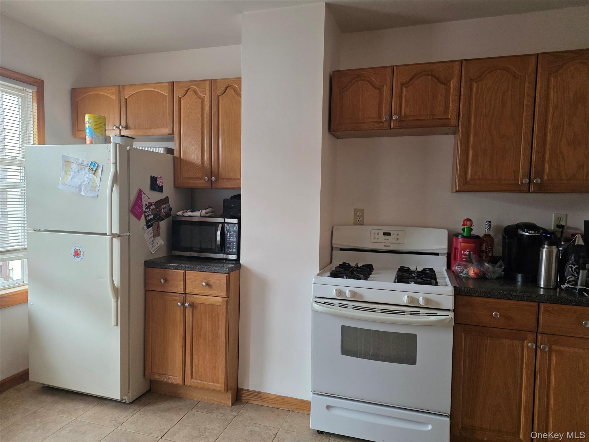 79-49 77th Road Queens, NY 11385 - Photo 5 of 12 Kitchen with white appliances, dark countertops, brown cabinets, and light tile patterned floors