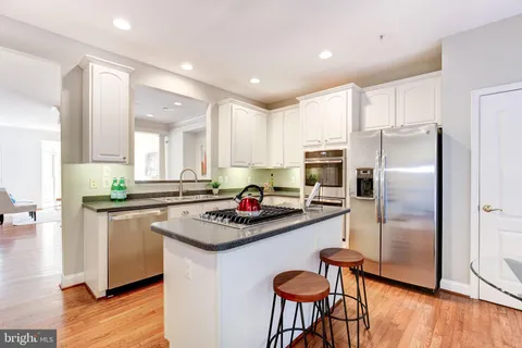 a kitchen with stainless steel appliances granite countertop a refrigerator a stove a sink a dining table and chairs with wooden floor