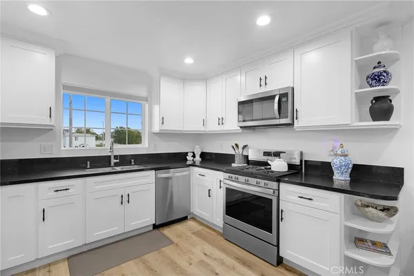 a kitchen with stainless steel appliances granite countertop white cabinets a sink a stove a microwave and a refrigerator