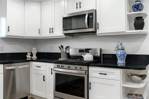 a kitchen with stainless steel appliances granite countertop white cabinets stove top oven and microwave