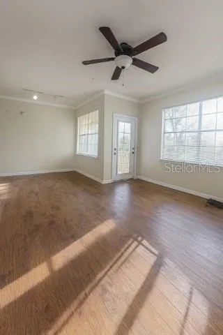 an empty room with wooden floor fan and windows
