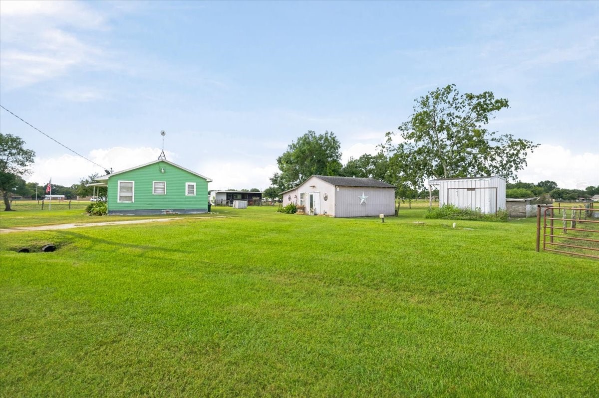 765 Norcross Road Wallis, TX 77485 - Photo 33 of 42 A charming rural property featuring a bright green house, a small shed, and a metal outbuilding, all set on a spacious, well-maintained grassy lot with open skies and a peaceful, country atmosphere.