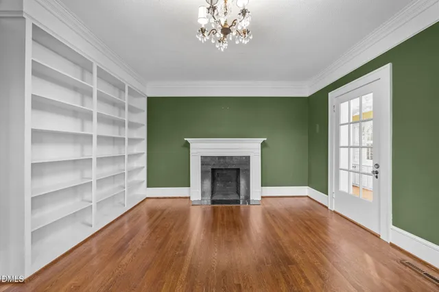 a view of an empty room with wooden floor fireplace and a window
