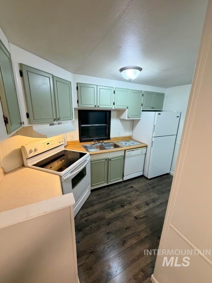 Kitchen with green cabinetry, white appliances, light countertops, dark wood finished floors, and exhaust hood