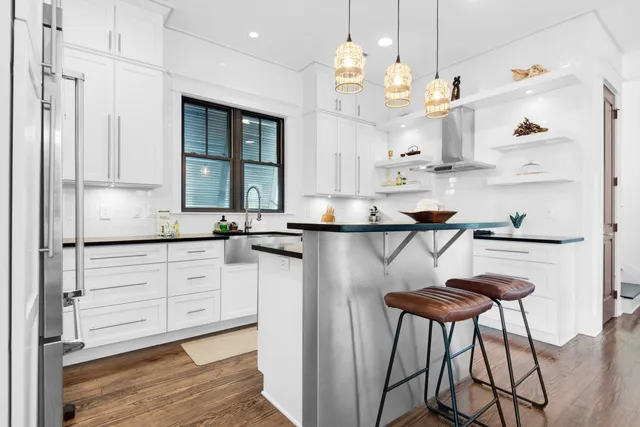 a very nice looking kitchen with granite countertop a stove a sink dishwasher and white cabinets with wooden floor
