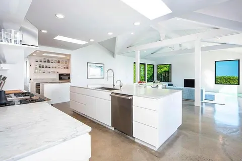 a large white kitchen with a large counter top space a sink stainless steel appliances and cabinets