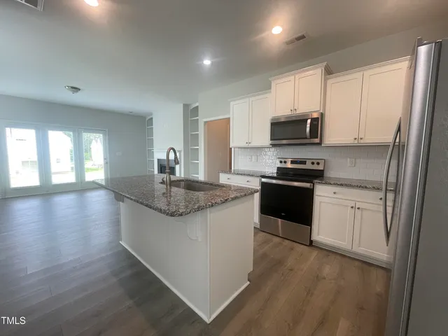 a large kitchen with stainless steel appliances granite countertop a stove top oven a refrigerator a sink and dishwasher with wooden floor