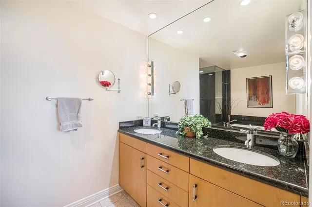 a bathroom with a granite countertop double vanity sink a mirror and shower