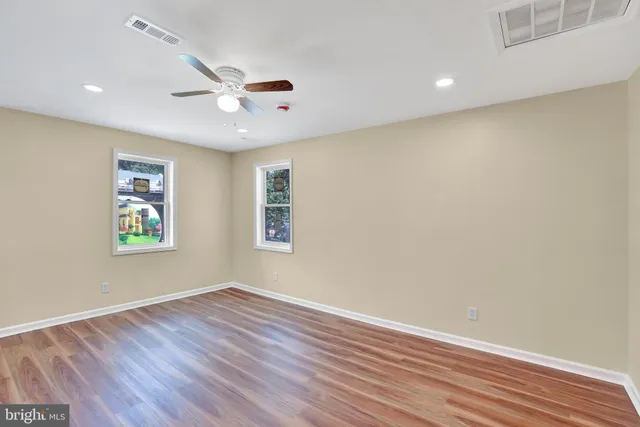 a view of an empty room with wooden floor and a ceiling fan