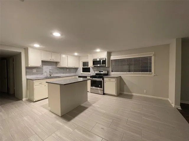 a large kitchen with kitchen island a sink a stove a oven a counter space and cabinets