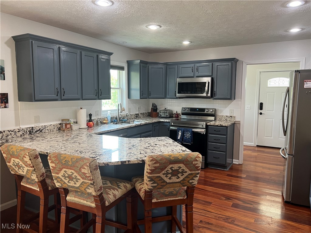 5912 Coen Road Vermilion, OH 44089 - Photo 7 of 28 Kitchen featuring stainless steel appliances, a peninsula, light stone countertops, a breakfast bar, and a textured ceiling