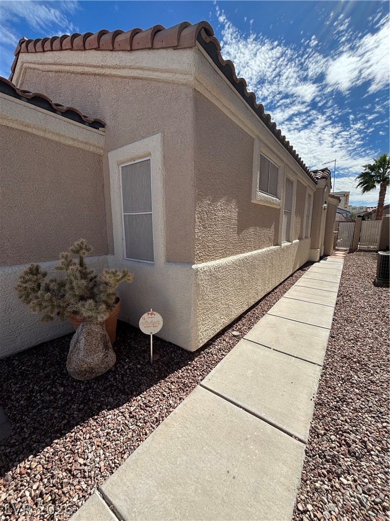 View of property exterior featuring a tiled roof, stucco siding, and a gate