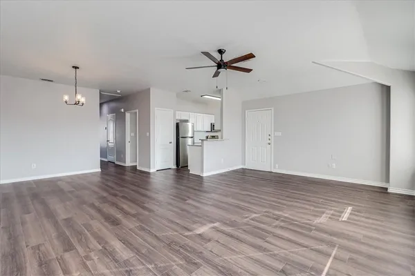a view of an empty room with wooden floor and a kitchen