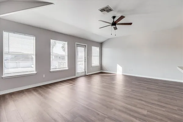 an empty room with wooden floor fan and windows