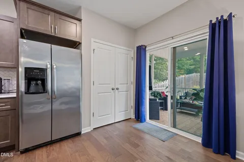a view of a refrigerator in kitchen and an empty room with wooden floor windows