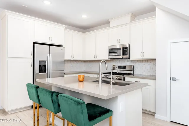 a large white kitchen with stainless steel appliances a stove a table and chairs
